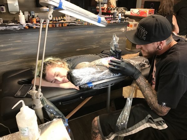 Harbor’s End tattoo artist Matt Vaught embellishes an existing tattoo on his assistant. 