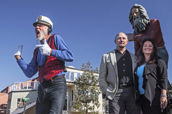 Filmmaker Martin and Tabitha Yewchuk, right, made a film about Laguna Beach’s greeters past and present. Michael Minutoli, left, takes up a role inhabited by Eiler Larsen, depicted in a sculpture at Brooks Street and Coast Highway. Photo by Mitch Ridder. 