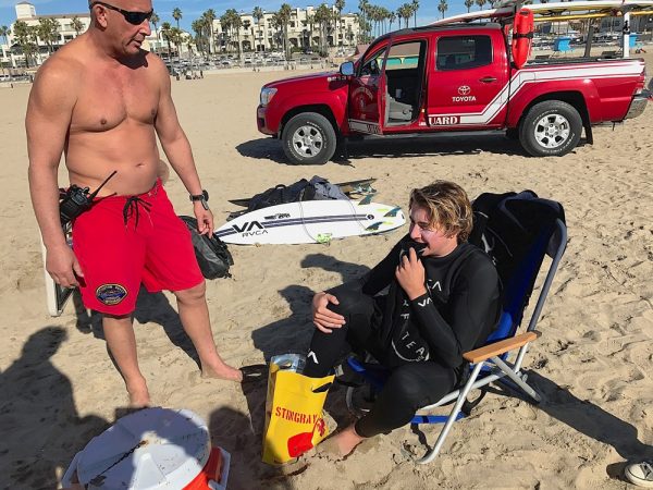A Huntington Beach lifeguard treats LBHS surf team competitor Noah North for a stingray injury. Another team member was also stung. Photos by Alisa Cairns.