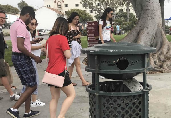 Laguna beachgoers stroll by a trash bin with the recycling divider left open. 